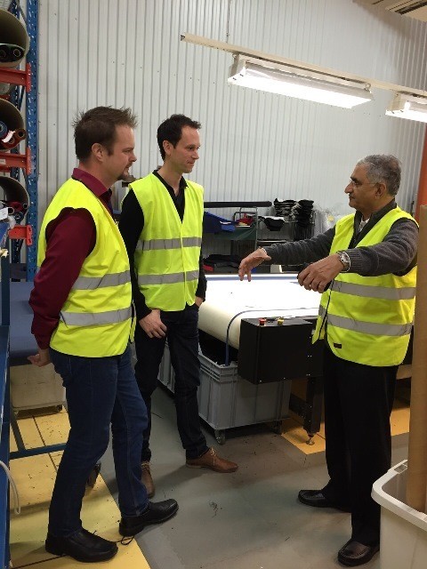 Sanjeev Baitmangalkar at a client's machine, talking through the work with two staff members; all three in high-visibility vests.